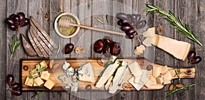 Cheese selection on wooden rustic board. Cheese platter with different cheeses, grapes, nuts, honey and dates on weathered wood b photo