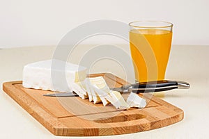 The cheese is sliced on a wooden cutting board and a glass of orange juice.