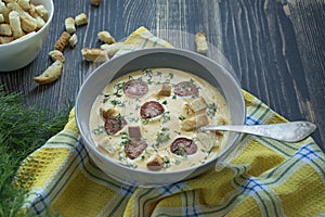 Cheese soup with grilled sausages and herbs. Cream soup served in a plate. Dark wooden background