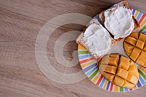 Cheese spread toasts with mango cut in cubes on a colorful plate on a wooden table