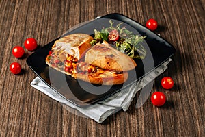 cheese steak sandwich with meat, vegetables, cheese and sauce served in the black tray on a dark wooden table. American street