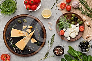 Cheese variety, olives and fresh herbs on grey background.