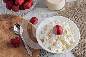 Cheese in white bowl with strawberries on wooden white table.
