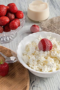 Cheese in white plate with strawberries on a wooden table with canvas tablecloth.