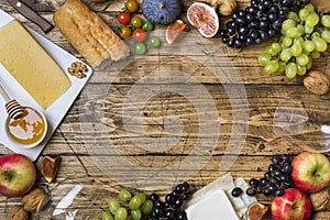 Cheese, wine, baguette grapes figs honey and snacks on the rustic wooden table top with copy space.