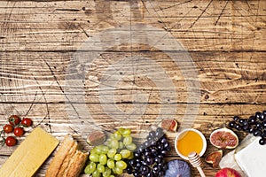 Cheese, wine, baguette grapes figs honey and snacks on the rustic wooden table top with copy space.