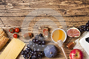 Cheese, wine, baguette grapes figs honey and snacks on the rustic wooden table top with copy space.