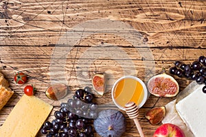 Cheese, wine, baguette grapes figs honey and snacks on the rustic wooden table top with copy space.