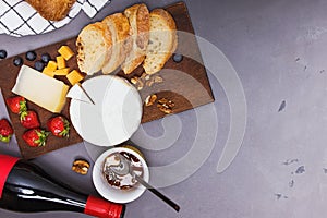 Cheese, wine bread and strawberries on grey stone table.