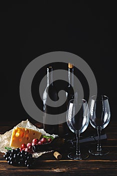Cheese wine and bunches of grapes on a black background