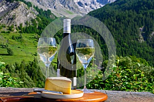 Cheese and wine, glasses of dry white Roussette de Savoie and Vin de Savoie wine from Savoy region with tomme cheese and view on