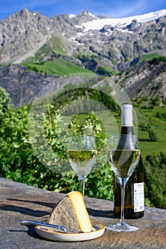 Cheese and wine, glasses of dry white Roussette de Savoie and Vin de Savoie wine from Savoy region with tomme cheese and view on