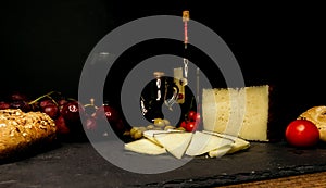 Cheese, wine, grapes, olives and tomatoes on a black background