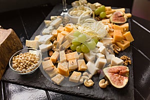 Cheeseboard or assorted of cheese. Abundance of gourmet cheeses with fig, grapes and nuts on black wooden plank