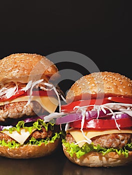 Cheeseburger with beef cutlets and fresh vegetables, composition: pepper, onion, tomatoes,egg, salad, cheese on a dark background.