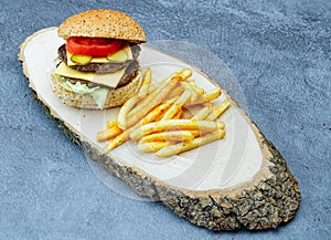 Cheeseburger with cheddar chese, pickled cucumbers, french fries on wooden tray