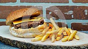 Cheeseburger with cheddar chese, russian salad, pickled cucumbers, french fries on wooden tray with brick wall background