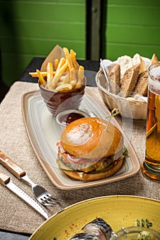 Cheeseburger with french fries and glass of beer on the table at restaurant