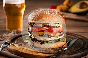 Cheeseburger, made from rye bun with tomato slice and melted cheese on a roasted beef, and lettuce leaf on a wooden