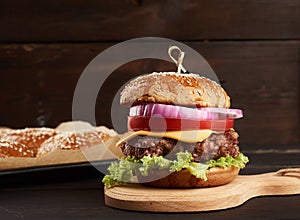 Cheeseburger with tomatoes, barbecue cutlet and sesame bun on an old wooden cutting board, brown background