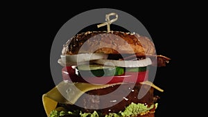 Cheeseburger with tomatoes, onions, barbecue cutlet and sesame bun on an old wooden cutting board, black background