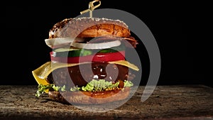 Cheeseburger with tomatoes, onions, barbecue cutlet and sesame bun on an old wooden cutting board, black background