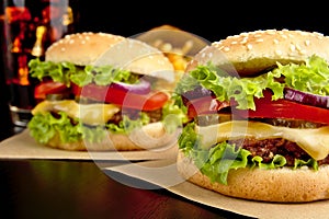 Cheeseburgers,french fries and cola on wooden desk on black