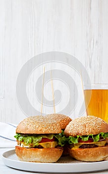 Cheeseburgers on grey plate and glass of beer. White wooden background. Side view.