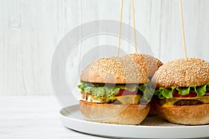 Cheeseburgers on grey plate. White wooden background. Side view. Close-up.
