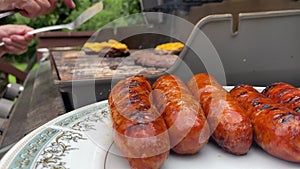 cheeseburgers and sausages on a backyard gas grill woman uses a patula and places the ready sausages on a serving plate