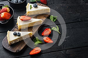 Cheesecake with blueberries and strawberries, on black wooden table background with copy space for text