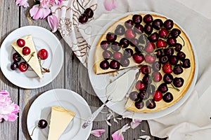 Cheesecake with cherry, two slices on saucers and metal tray on a wooden table. .