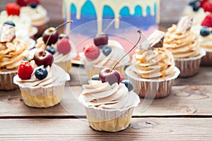 Cheesecake cupcake with cream cheese frosting and fresh cherry on top, wooden background