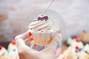 Cheesecake cupcake with cream cheese frosting and fresh cherry on top, wooden background