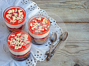 Cheesecake dessert in glass jar on wooden background.: chocolate biscuit, salted caramel, strawberry jelly, cheese mousse, chocola