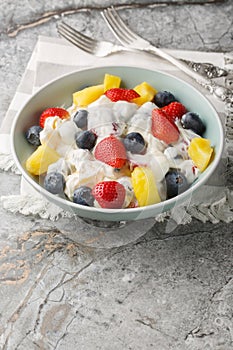 Cheesecake fruit salad with strawberries, blueberries, pineapple close-up in a bowl. Vertical