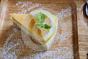 Cheesecake pie slice topped with lemon syrup and mint leaf on a wooden plate,