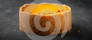 Cheesecake with yellow mango flavored layer decorated with red crumbs of freeze-dried raspberries on dark marble background.