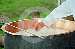 cheesemaker checks with hand the milk's temperature inside the c