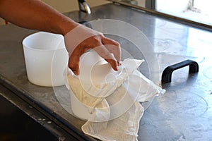 Cheesemaker placing top lid on a mold with porous cloth to press the cheese.