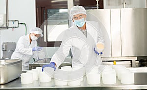 Cheesemaker in protective mask working in shaping workshop of cheese factory