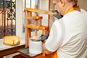 cheesemaker puts cheese under press, whey. Home production, business, portrait