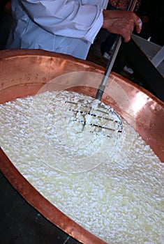 Cheesemaker stirs the curds into the big copper cauldron