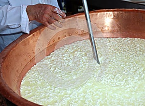 Cheesemaker stirs the curds into the cauldron to make cheese