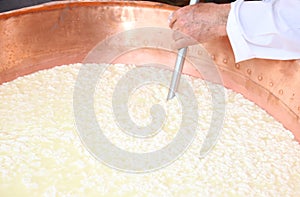 Cheesemaker stirs the curds into the copper cauldron to make che