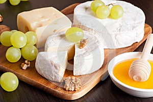 Cheeses, grapes and walnuts on a wooden background, horizontal