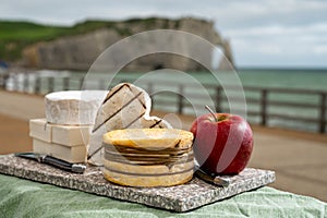 Cheeses of Normandy, round camembert cow cheese, yellow livarot, heartshaped neufchatel and view on alebaster cliffs Porte d`Aval