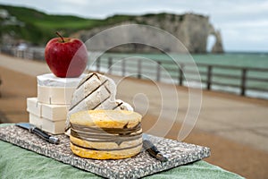 Cheeses of Normandy, round camembert cow cheese, yellow livarot, heartshaped neufchatel and view on alebaster cliffs Porte d`Aval