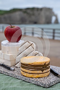 Cheeses of Normandy, round camembert cow cheese, yellow livarot, heartshaped neufchatel and view on alebaster cliffs Porte d`Aval