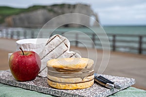 Cheeses of Normandy, round camembert cow cheese, yellow livarot, heartshaped neufchatel and view on alebaster cliffs Porte d`Aval